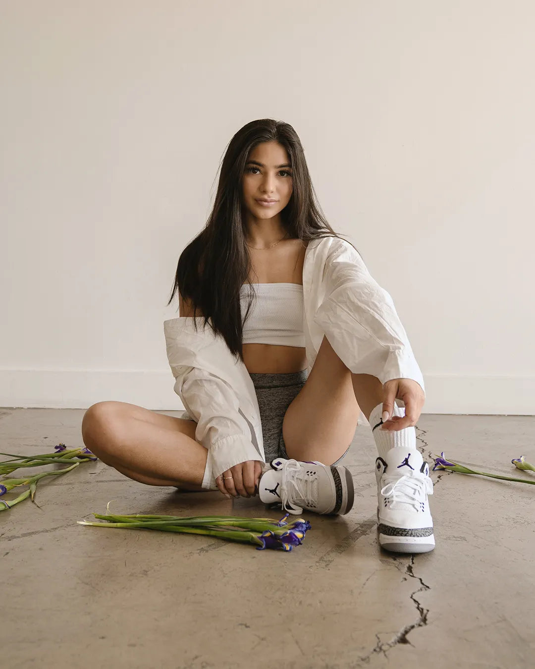 A girl sitting on the floor, surrounded by flower pedals, showing off her shoes. 