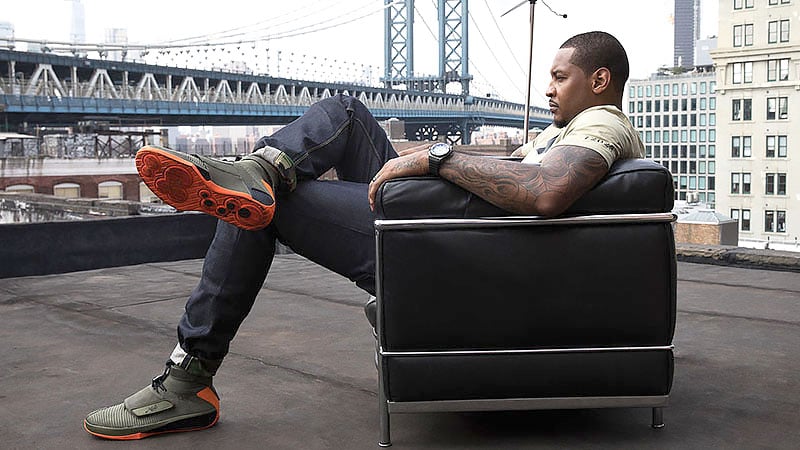 A man on the roof of a building, with a city skyline background, showing off his shoes.